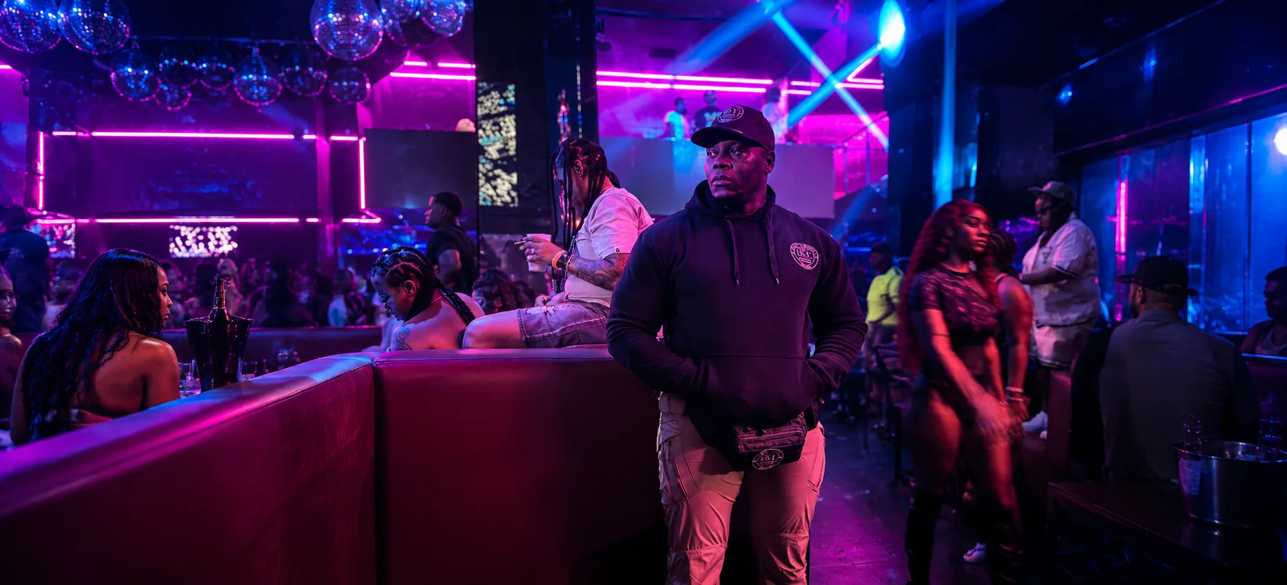 Security guard inside a vibrant neon nightclub with VIP guests around him