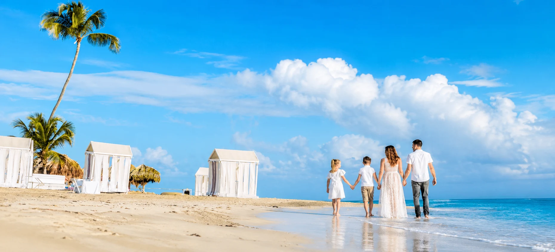 Family walking along a Punta Cana beach beside white cabanas and palm trees