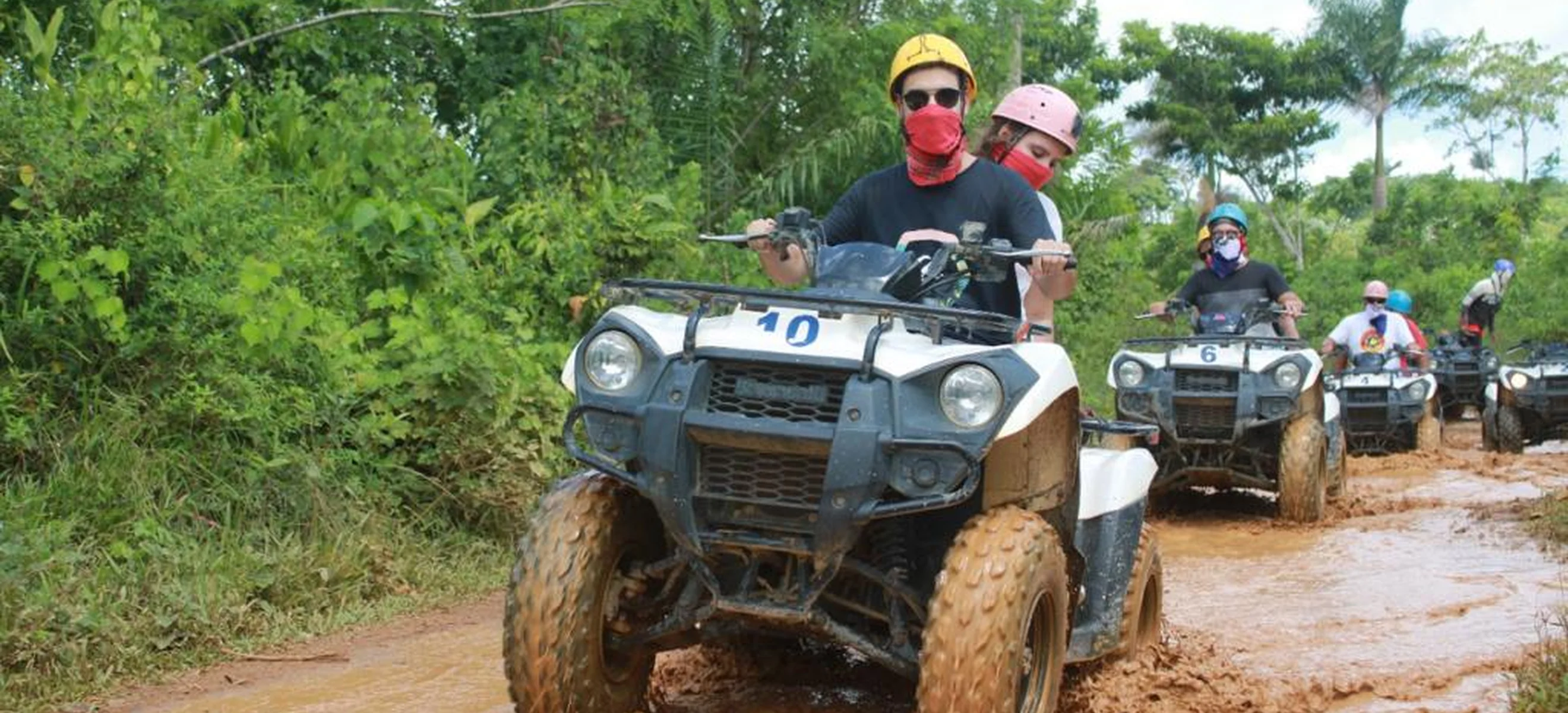 A guest drives an ATV through a clear shallow river during a Punta Cana off-road adventure through tropical scenery and countryside trails.