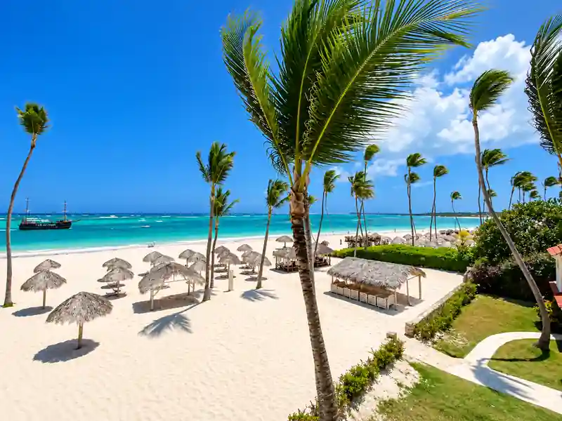 Tropical Punta Cana beach with palm trees, turquoise Caribbean water and thatched umbrellas