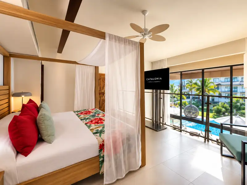 Catalonia Punta Cana resort room with canopy bed and tropical pool view.